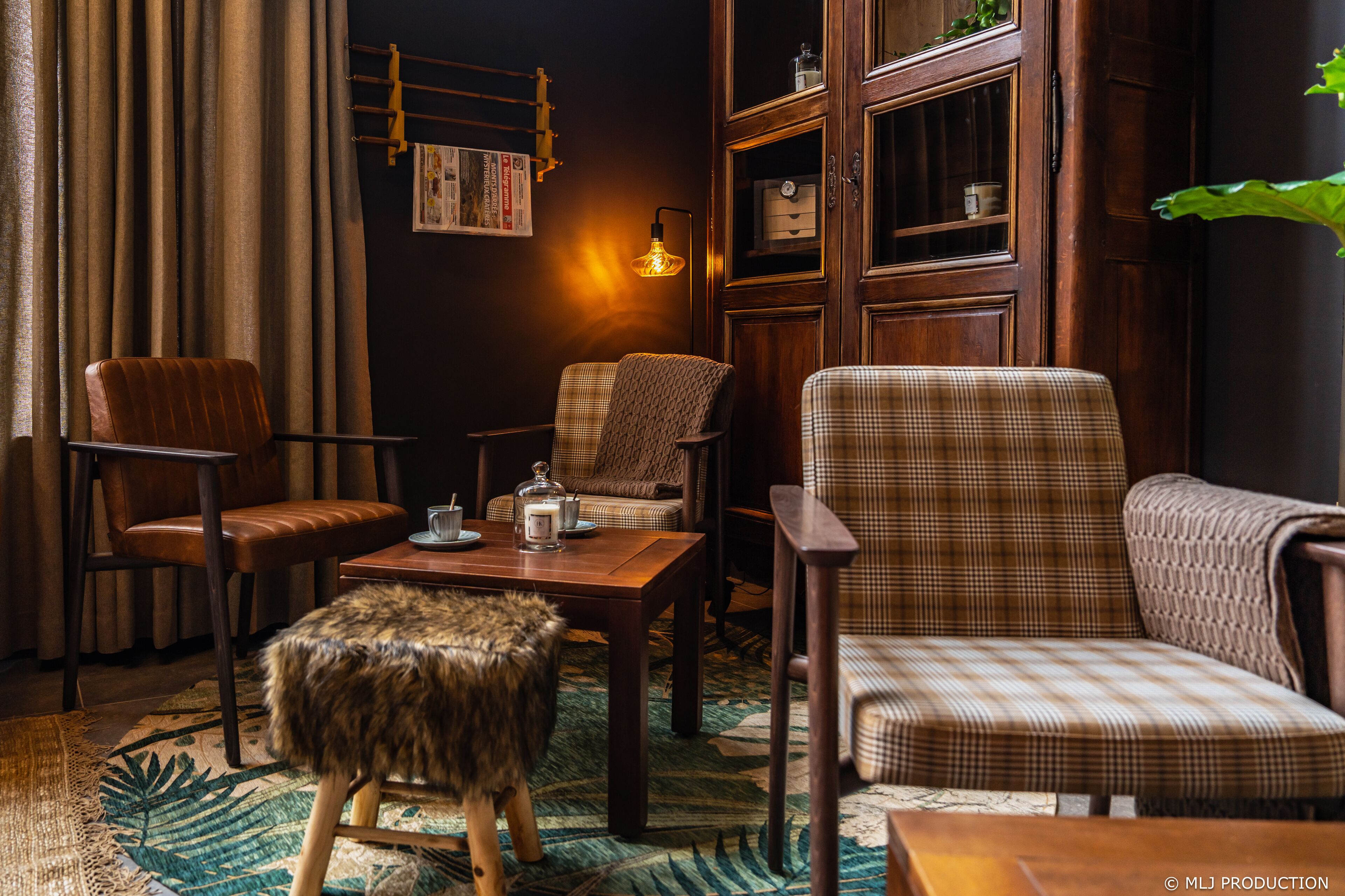 A cozy room with a wooden coffee table, two patterned armchairs, a leather chair, a fur-covered ottoman, and a wall-mounted lamp.