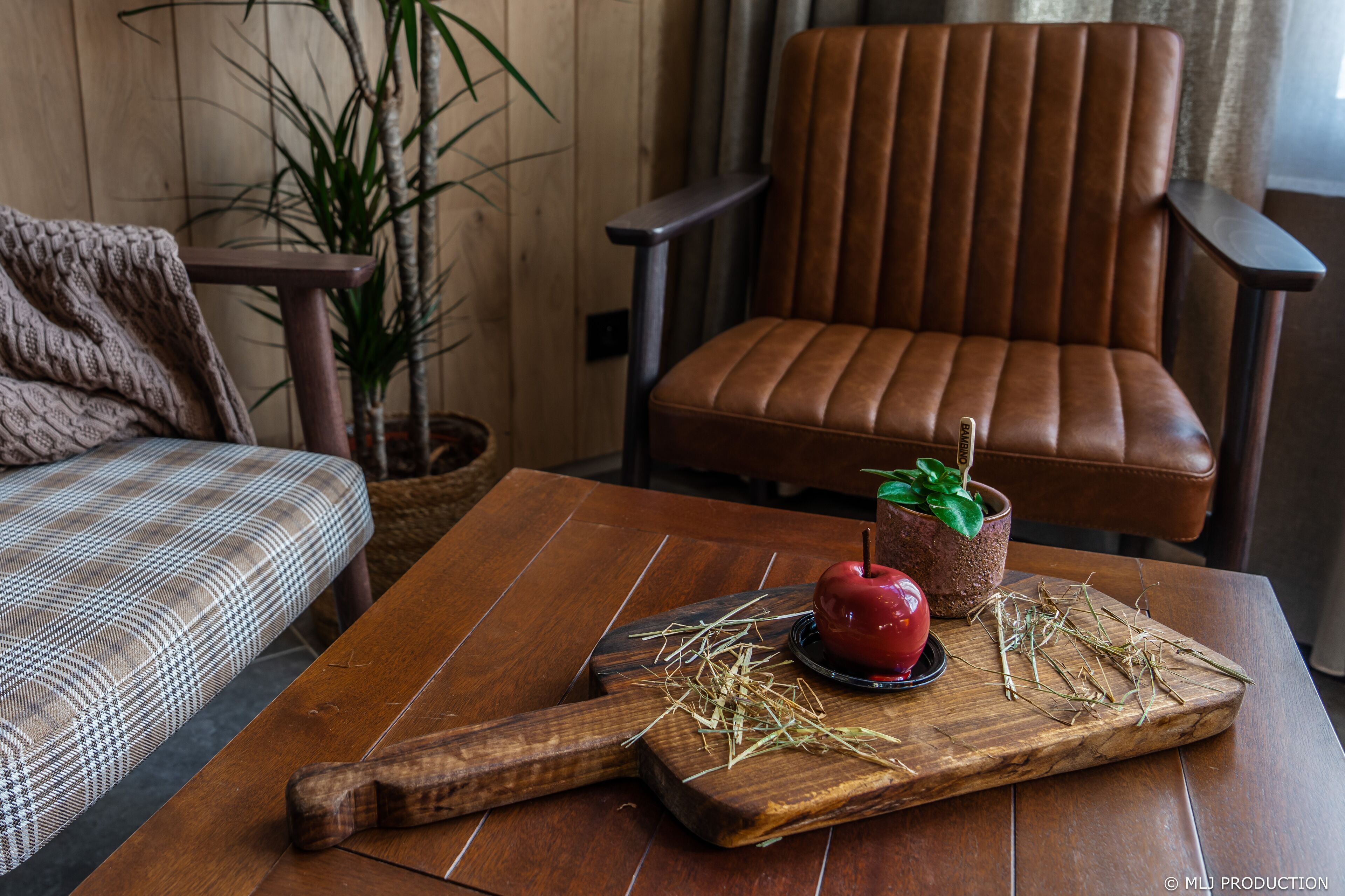 A wooden table with a cutting board, a red apple, and a potted plant.