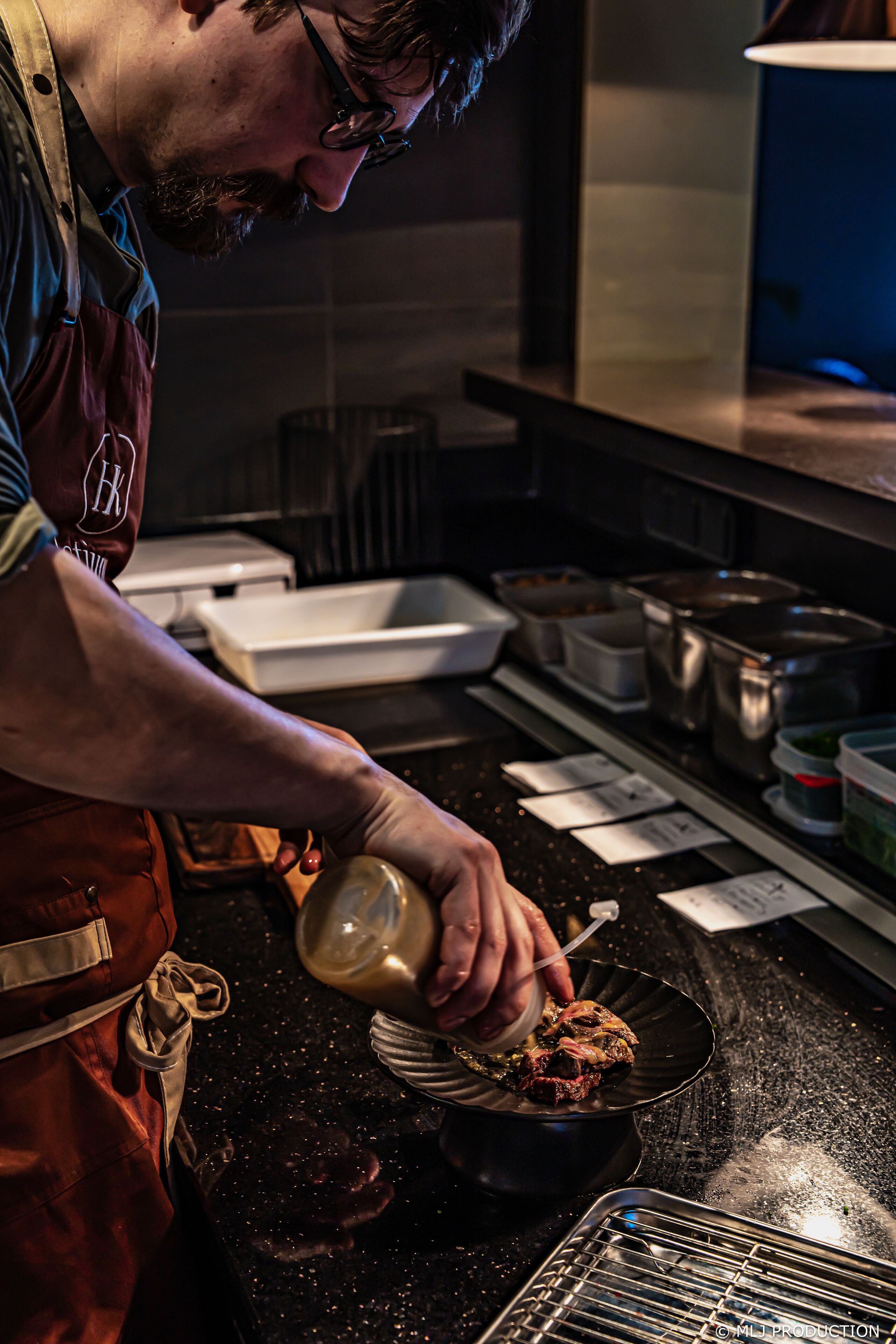 A person in an apron preparing food in a kitchen with various cooking utensils and containers.