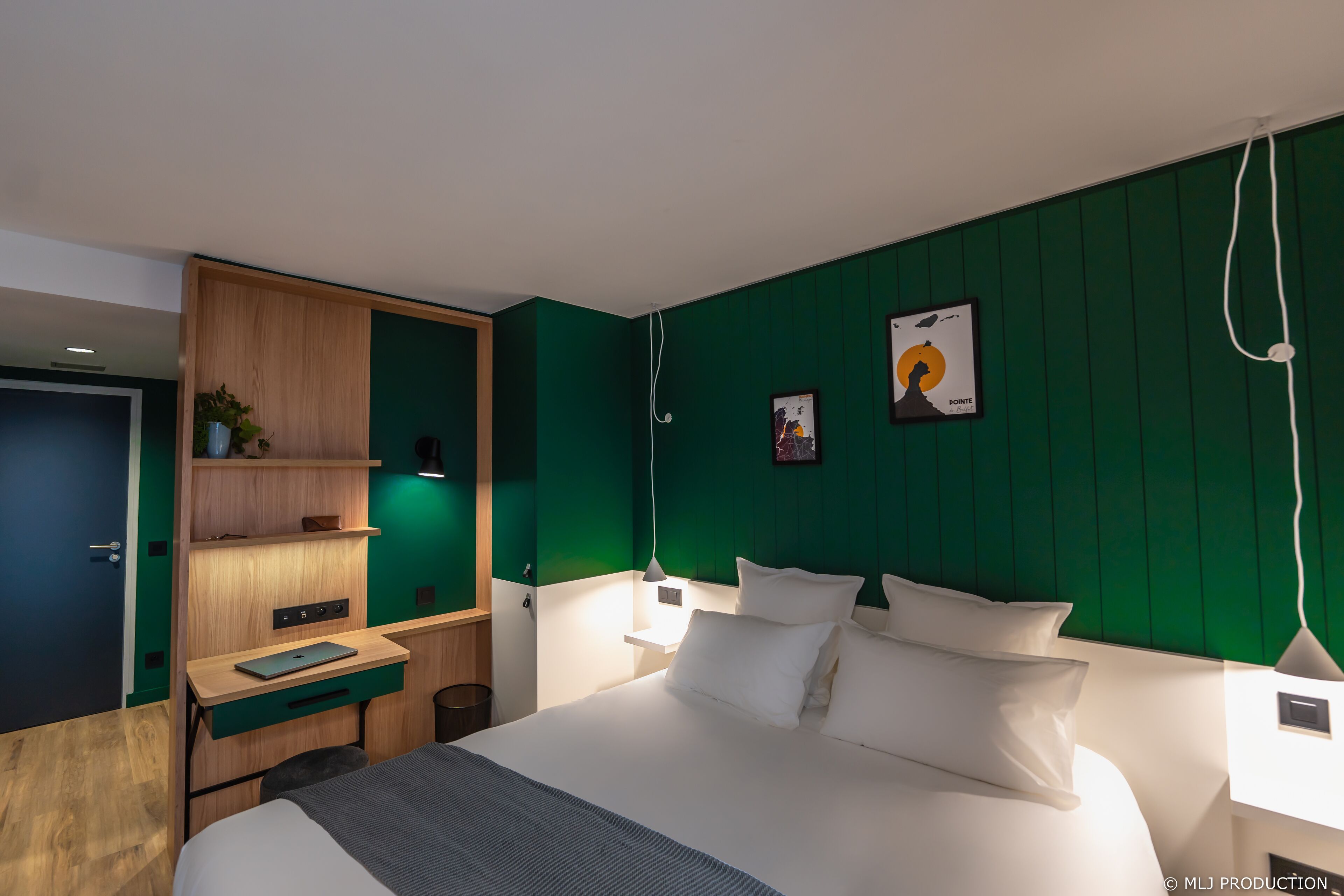 A modern hotel room with a bed, a desk, a wardrobe, and green walls.