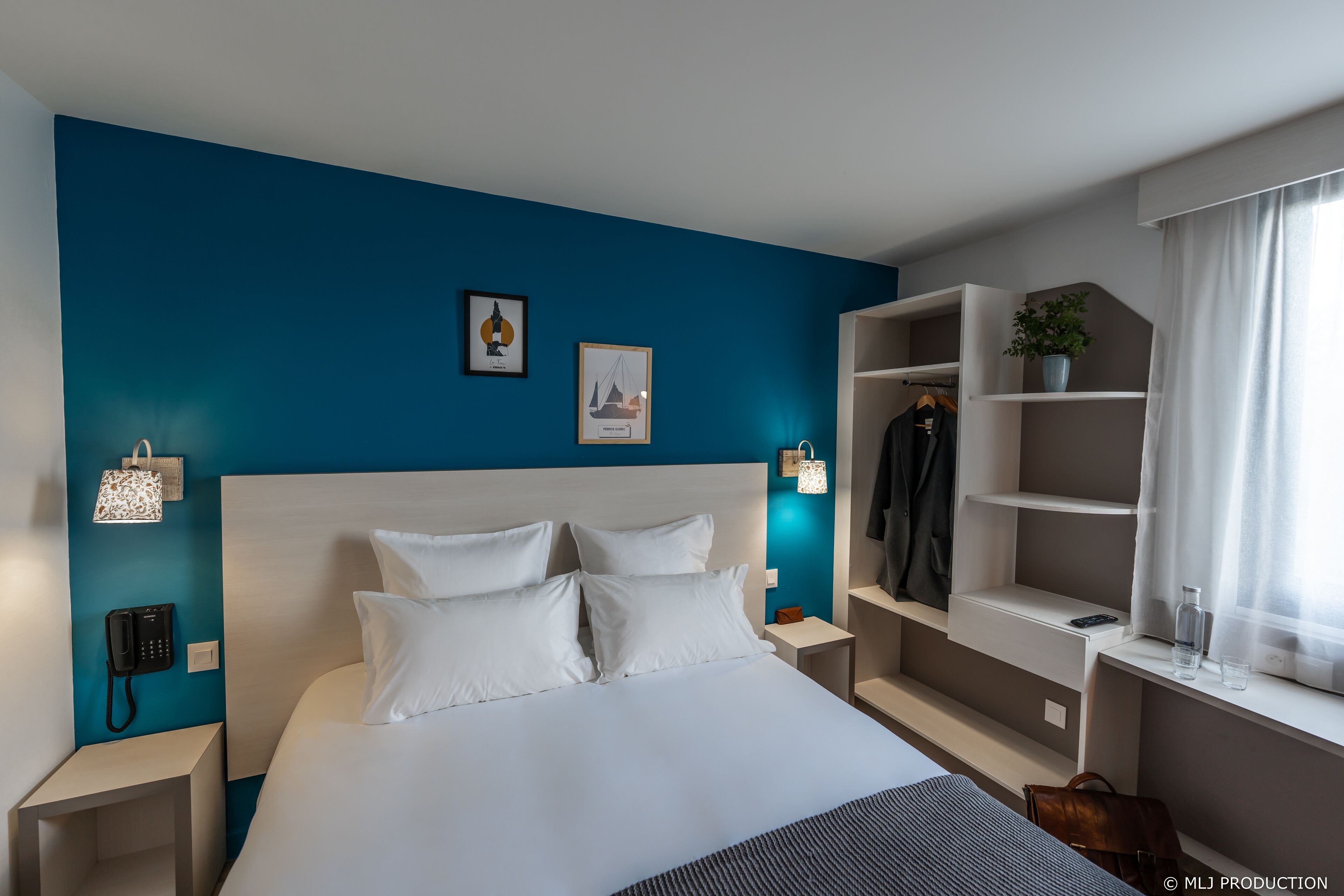 Una habitación de hotel moderna con una cama grande, un armario, una mesita de noche con lámpara y un teléfono en la pared.