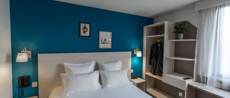 Una habitación de hotel moderna con una cama grande, un armario, una mesita de noche con lámpara y un teléfono en la pared.