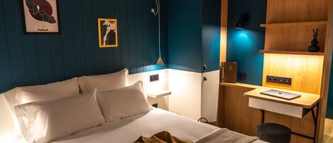 Ein Hotelzimmer mit einem Bett, Nachttischen, einem Schreibtisch mit einem Laptop, einem Stuhl und Wandbildern.