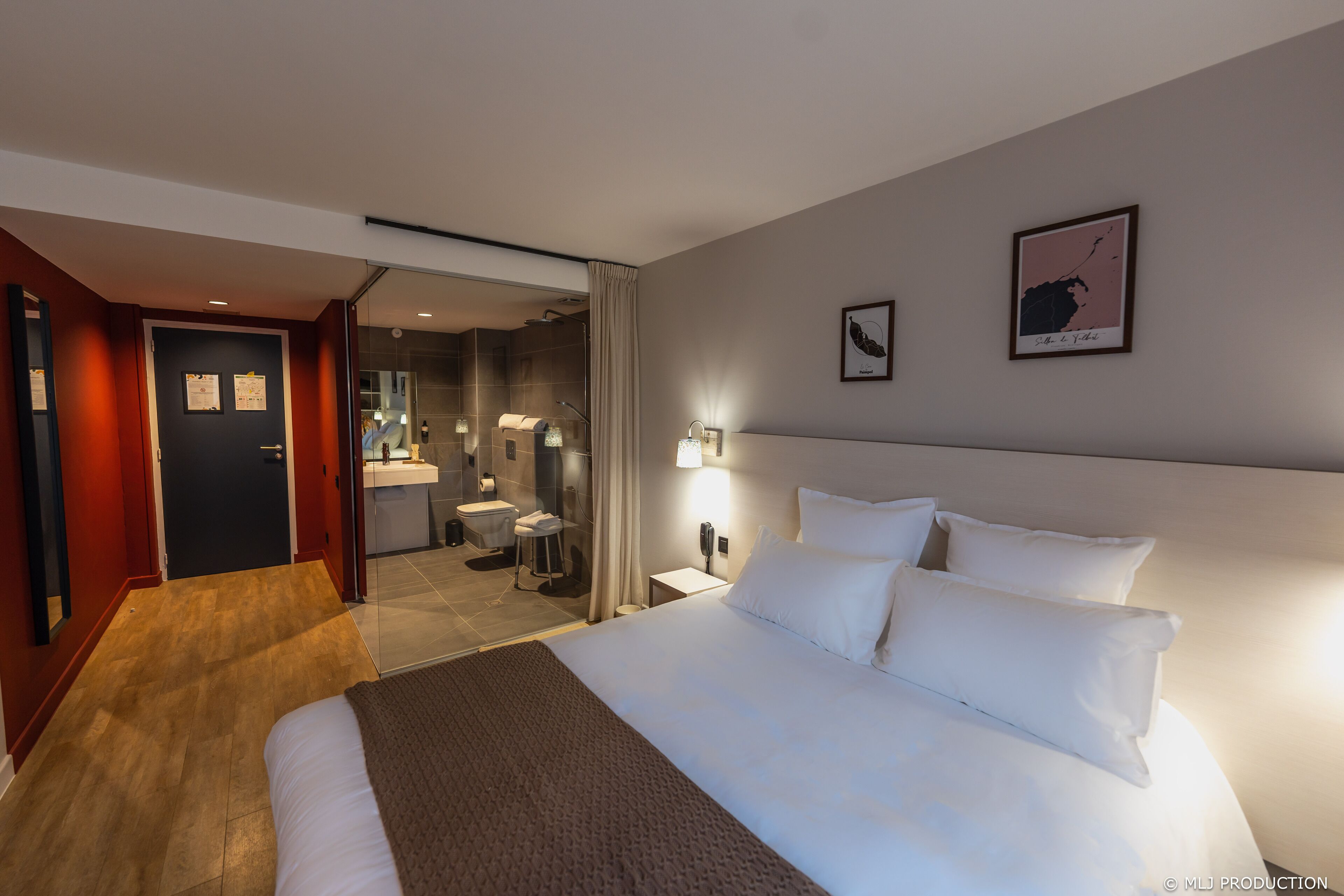 A modern hotel room with a large bed, a bathroom with a glass shower, and a small sitting area.