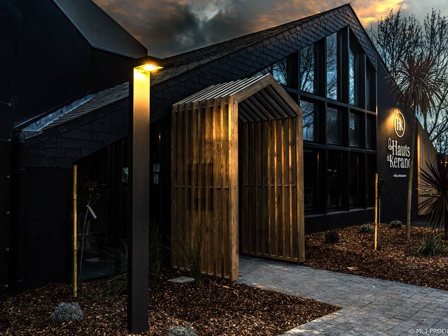 Un bâtiment moderne avec une structure en bois à l’avant, une enseigne indiquant « Hauts Kerans » et un chemin menant à l’entrée.