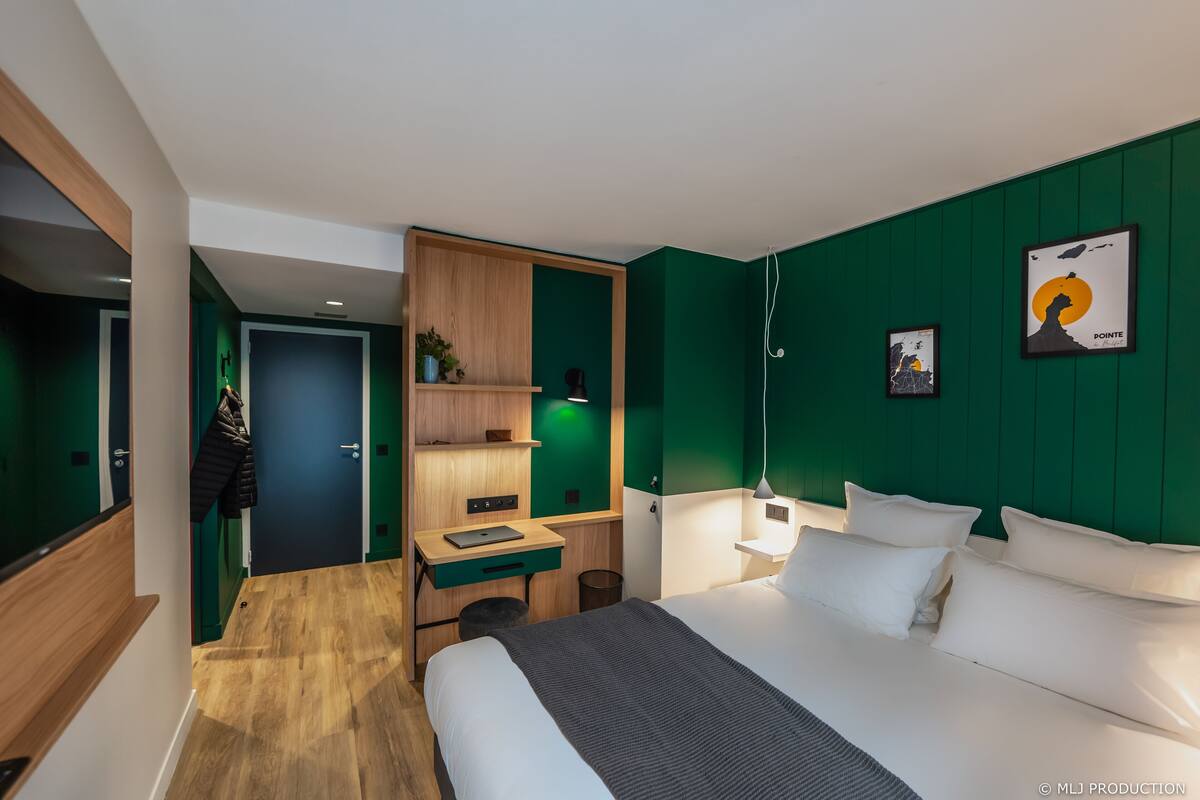 Ein modernes Hotelzimmer mit Bett, Schreibtisch und einer Wand in Grünton.
