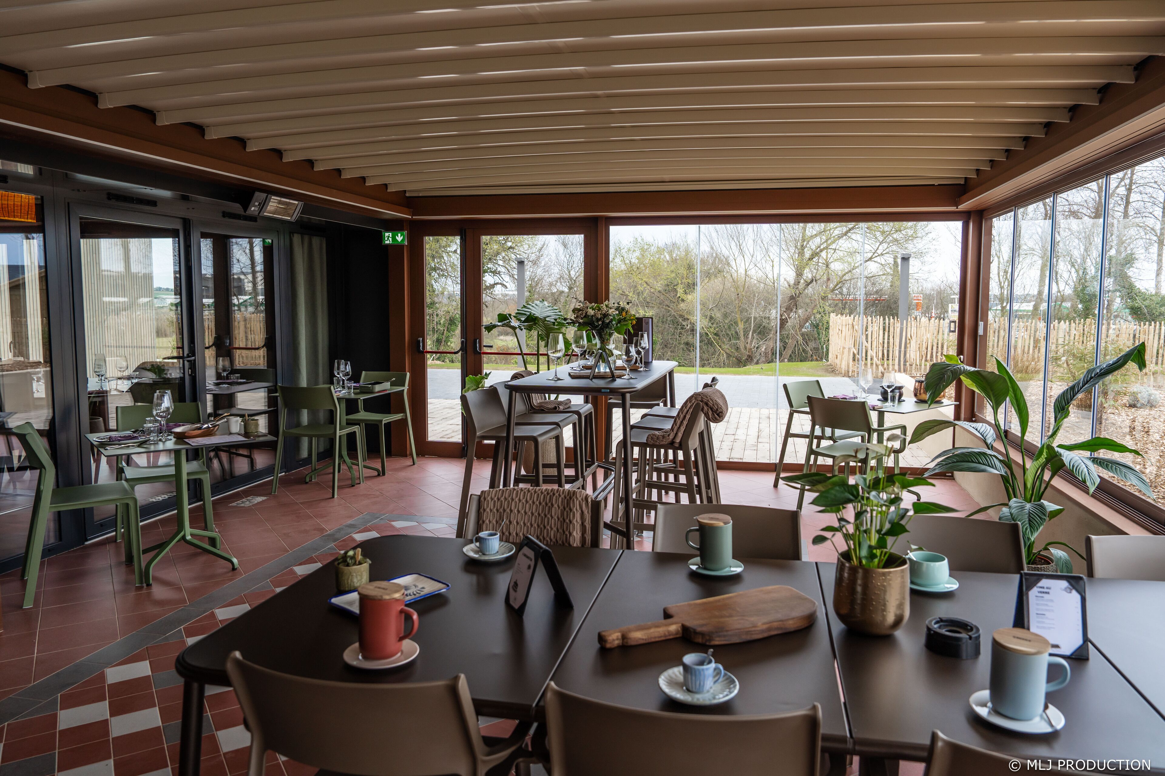 A modern dining area with tables and chairs, large windows, and potted plants.