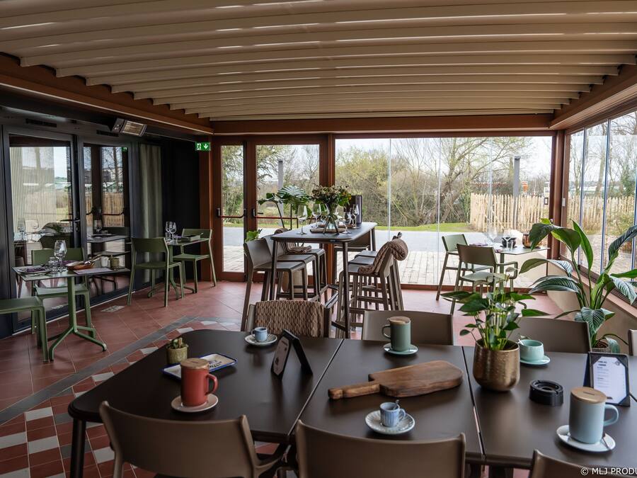 A modern dining area with tables and chairs, large windows, and potted plants.