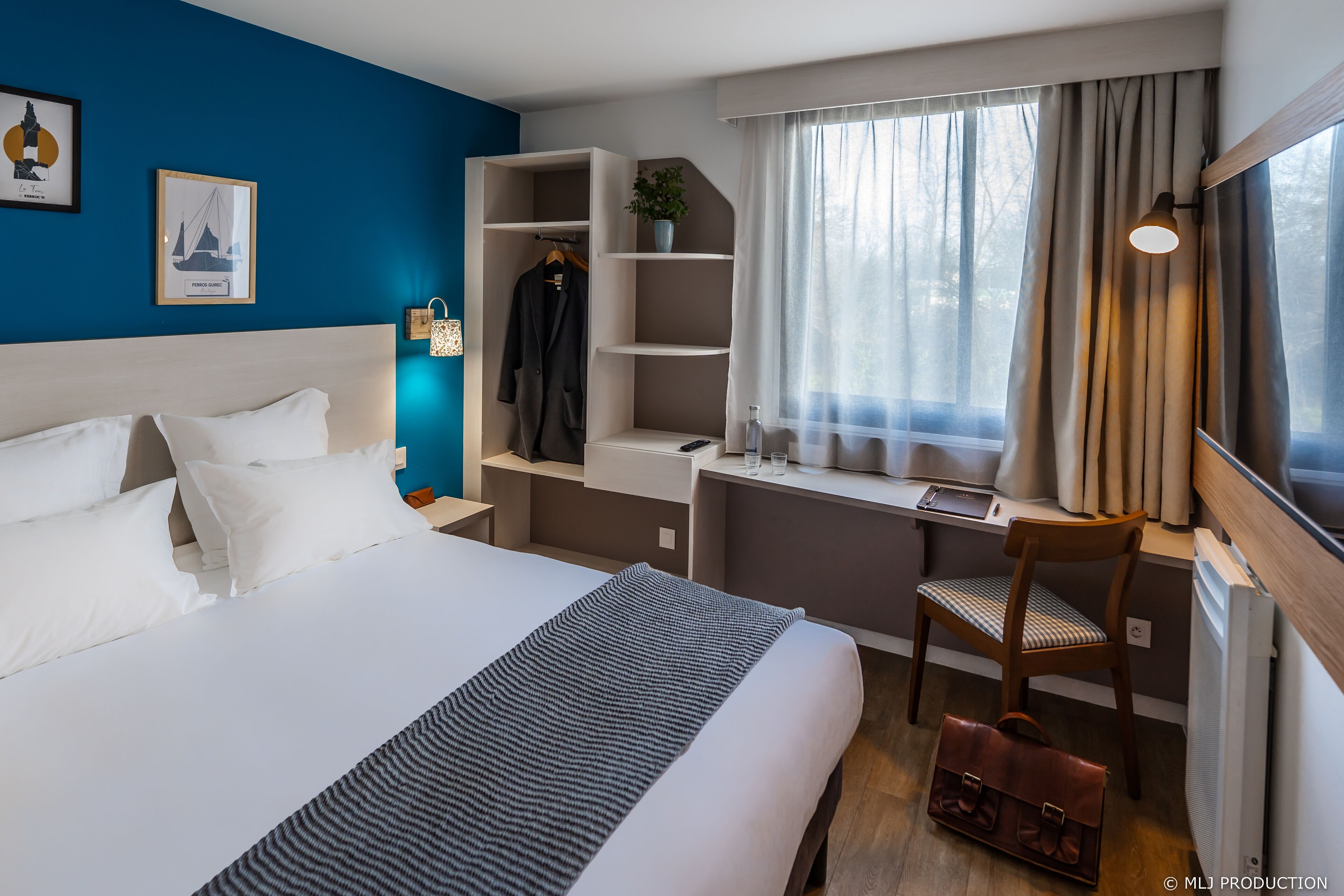 A hotel room with a bed, a desk, a chair, a wardrobe, and a window with curtains.