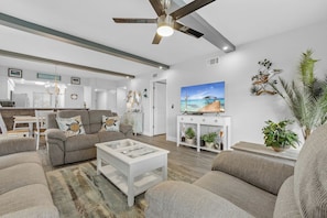 A modern living room with a ceiling fan, a television, and a painting of a beach scene.
