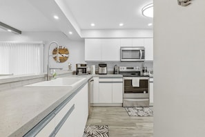 A modern kitchen with white cabinetry, stainless steel appliances, and a large wall clock.
