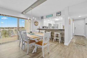 A modern kitchen with a central island, white cabinetry, and a view of the outdoors through large windows.