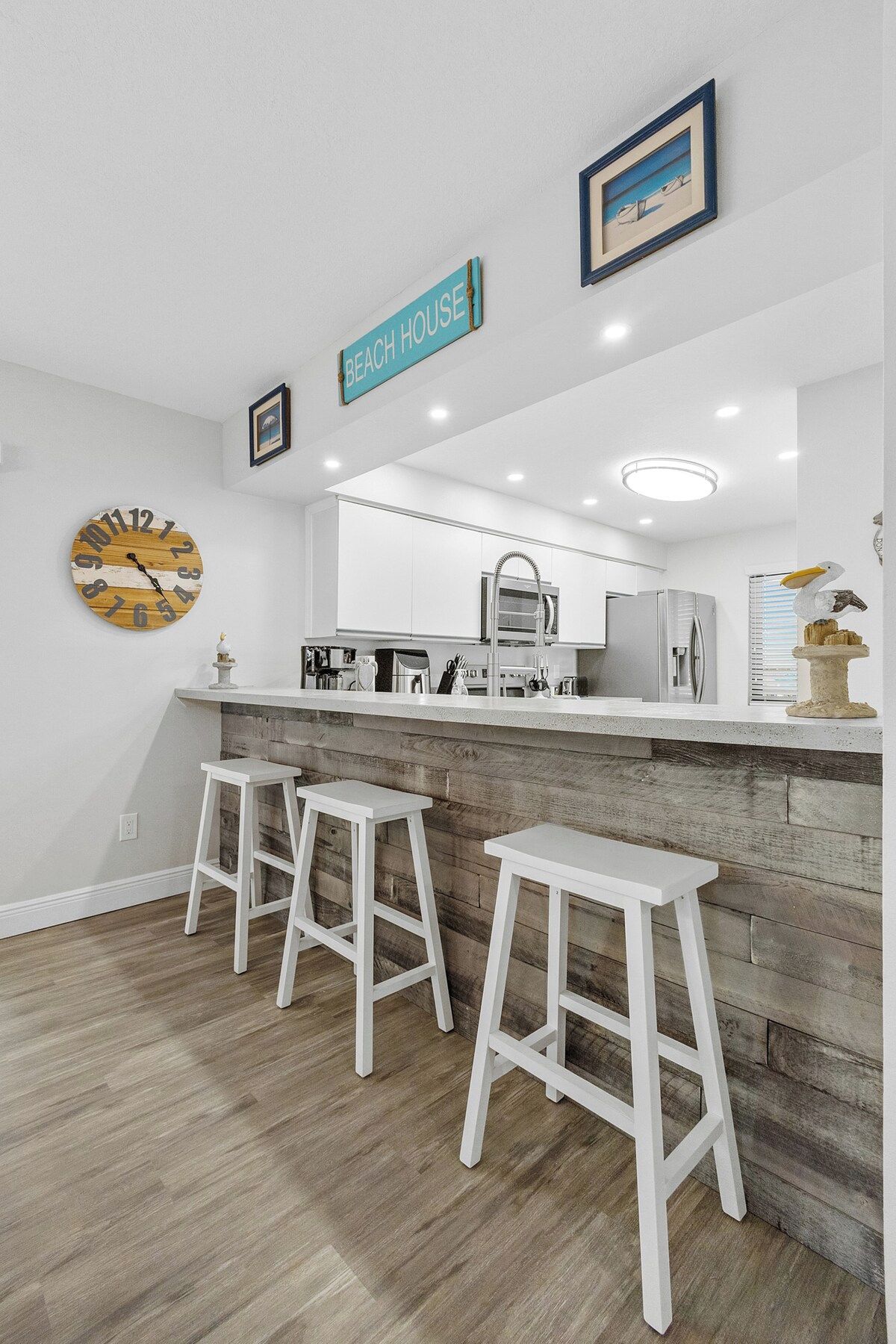 A modern kitchen with white cabinetry, a wooden countertop, and a bar area with white stools.