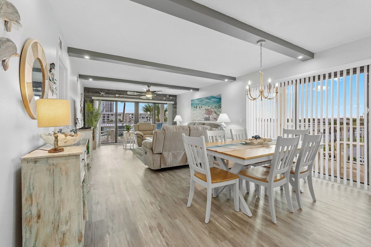 A spacious living area with a dining table and chairs, a sofa, and a view of the outdoors.