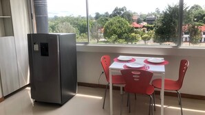 Une cuisine équipée d’un réfrigérateur en acier inoxydable, une table à manger avec des chaises rouges et une fenêtre donnant sur des arbres et des immeubles.