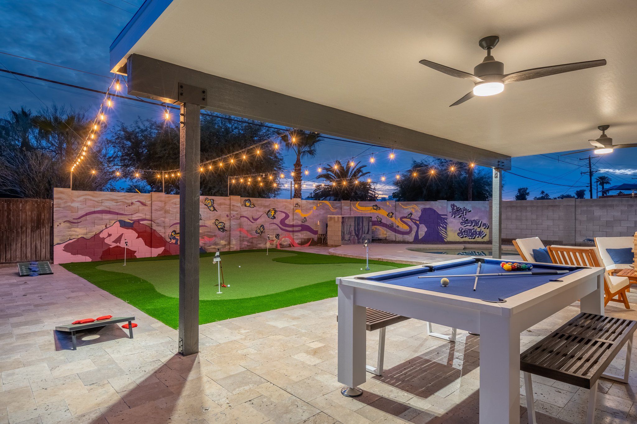 Área de piscina externa com mural, luzes de corda e ventilador de teto.