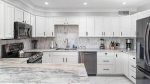 A modern kitchen with white cabinets, a marble countertop, stainless steel appliances, and a central island. - Pool & Art Lover Oasis near Old Town w/ Mini Golf (Scottsdale)