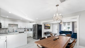 A modern kitchen with white cabinets, a large island, and a dining area with a wooden table and chairs. - Pool & Art Lover Oasis near Old Town w/ Mini Golf (Scottsdale)
