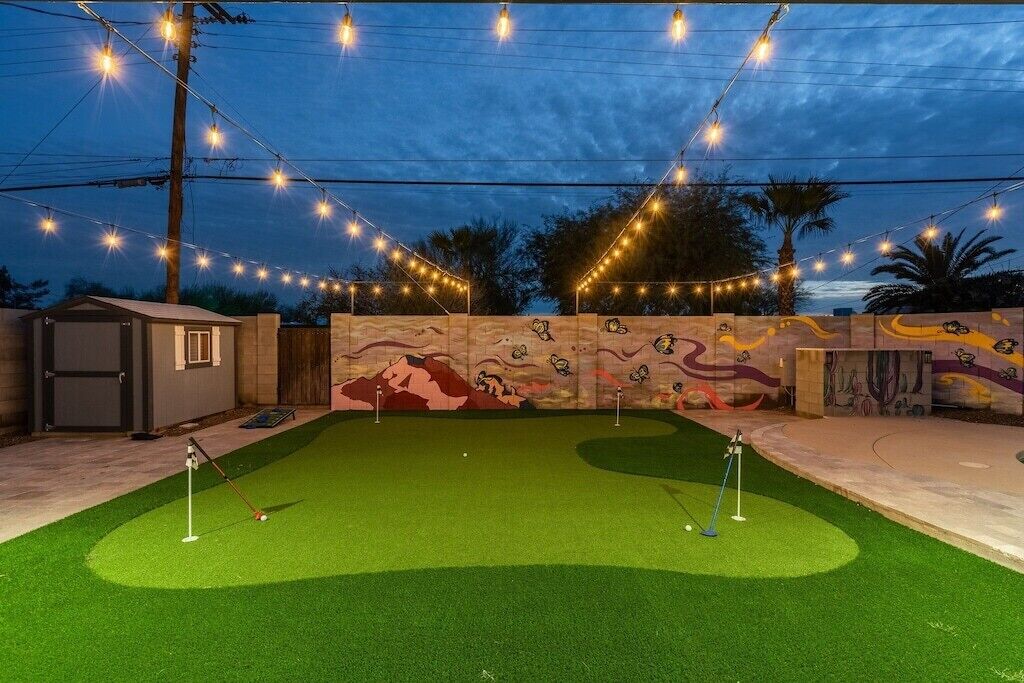 Ein Golfplatz im Abenddämmerung mit Lichterketten und einem Wandgemälde.