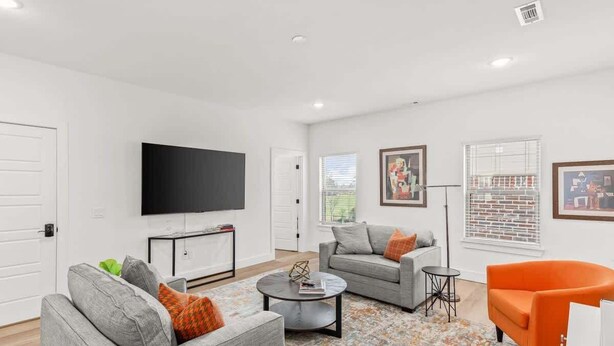 A modern living room with a flat-screen TV, grey sofas, a coffee table, and an orange armchair. - Art-Lover’s Suite - Minutes to Crystal Bridges (Bentonville)