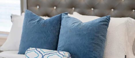 A bed with a tufted headboard, two blue pillows, and a patterned pillow.