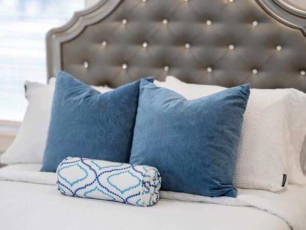 A bed with a tufted headboard, two blue pillows, and a patterned pillow.