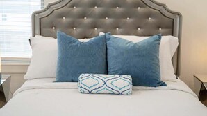 A bed with a tufted headboard, two blue pillows, and a patterned pillow on a white bedspread. - Art-Lover’s Suite - Minutes to Crystal Bridges (Bentonville)