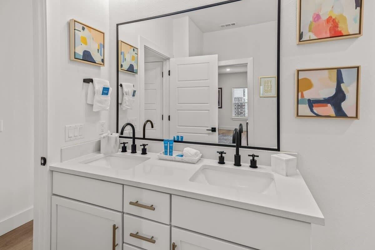 A modern bathroom with a white vanity, two sinks, black faucets, and a large mirror.