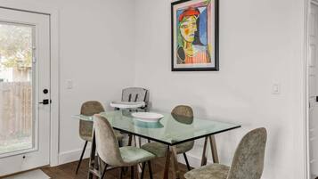 A dining area with a glass table, four chairs, and a framed artwork on the wall.