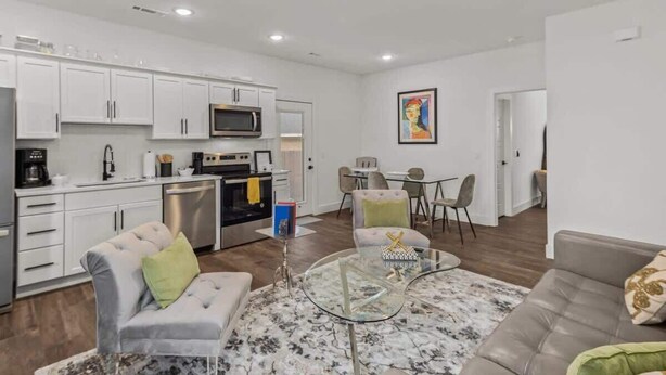 A modern kitchen with white cabinets, a microwave, and a dining area with a table and chairs. - Bentonville Art Suite • Near Crystal Bridges & Osage Park (Bentonville)