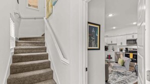 A staircase leading to a kitchen with white cabinets and a gray sofa. - Bentonville Art Suite • Near Crystal Bridges & Osage Park (Bentonville)