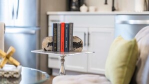 A dining table with a cake stand holding books and a cake. - Bentonville Art Suite • Near Crystal Bridges & Osage Park (Bentonville)