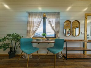 Une pièce avec une fenêtre, deux fauteuils de couleur turquoise, une table en bois, une plante en pot et un miroir.