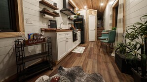 Eine moderne Küche mit Holzausstattung, einem eingebauten Backofen und einer Mikrowelle. Ein Essbereich mit Tisch und Stühlen sowie eine Topfpflanze sind ebenfalls vorhanden.