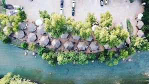 An aerial view of a riverside area with thatched-roof huts and a parking lot. - Son's Guadalupe Glamping Tent E (New Braunfels)