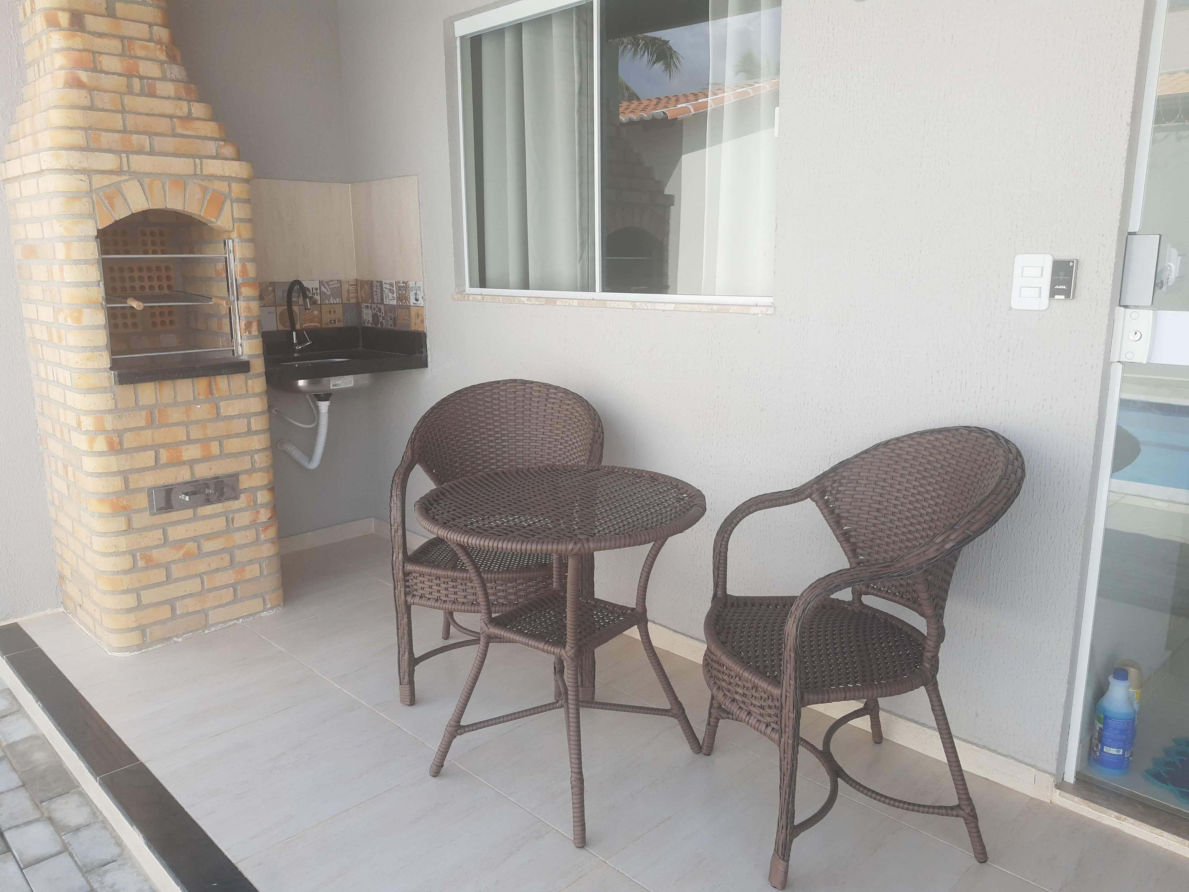 Un patio con un horno de ladrillo, dos sillas de mimbre, una mesita y una ventana con vistas a palmeras.