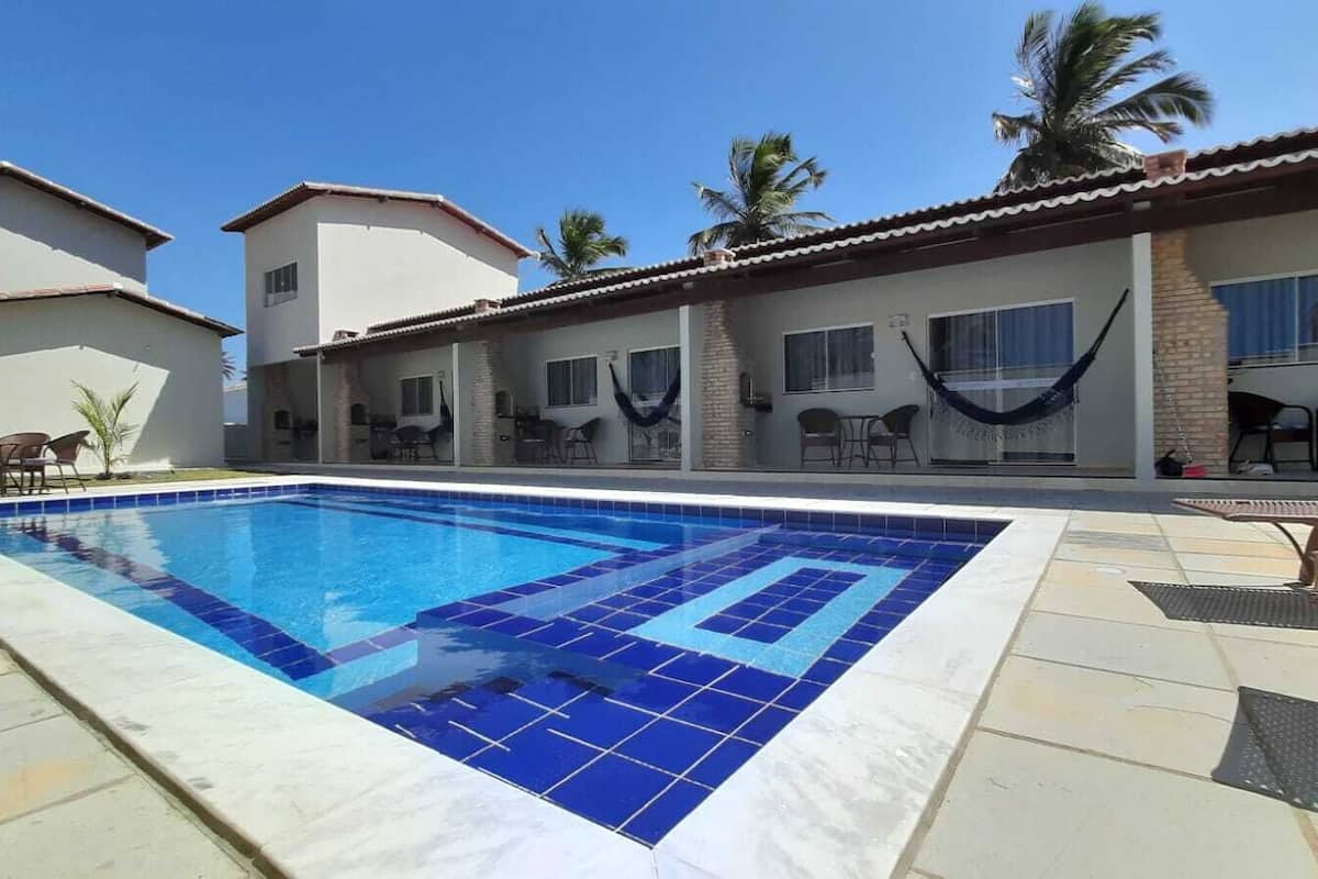Une piscine aux carreaux bleus, entourée de mobilier d’extérieur et de palmiers.