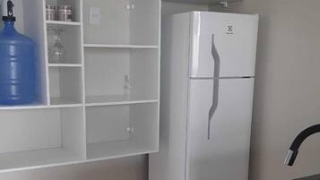 Una cocina con armarios blancos, encimera negra y refrigerador blanco.