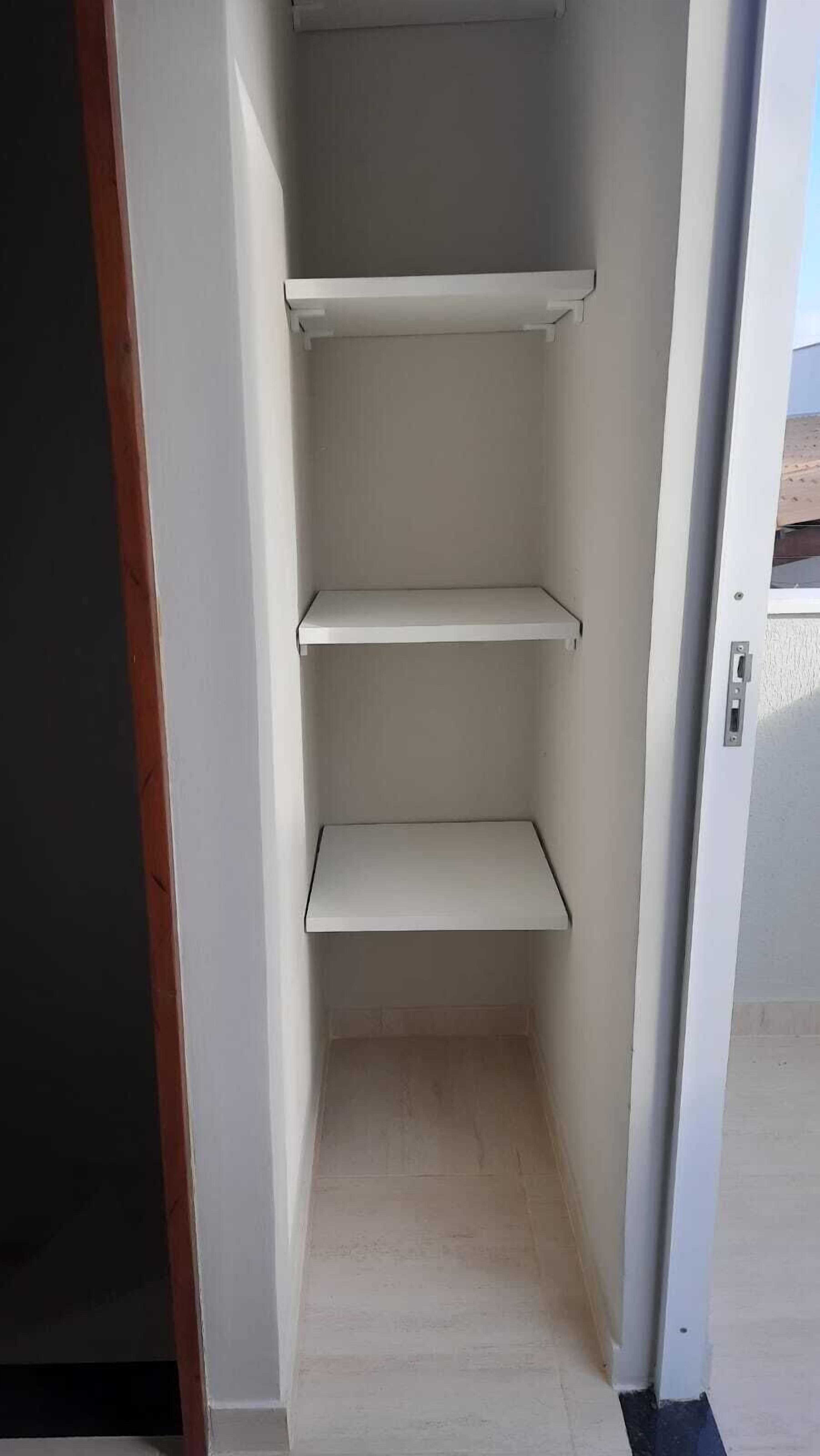 Un espace intérieur étroit et blanc, doté de trois étagères et d’une porte.