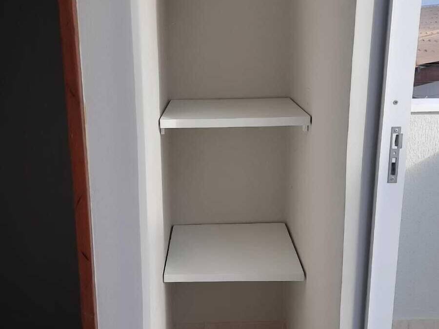 Un espace intérieur étroit et blanc, doté de trois étagères et d’une porte.
