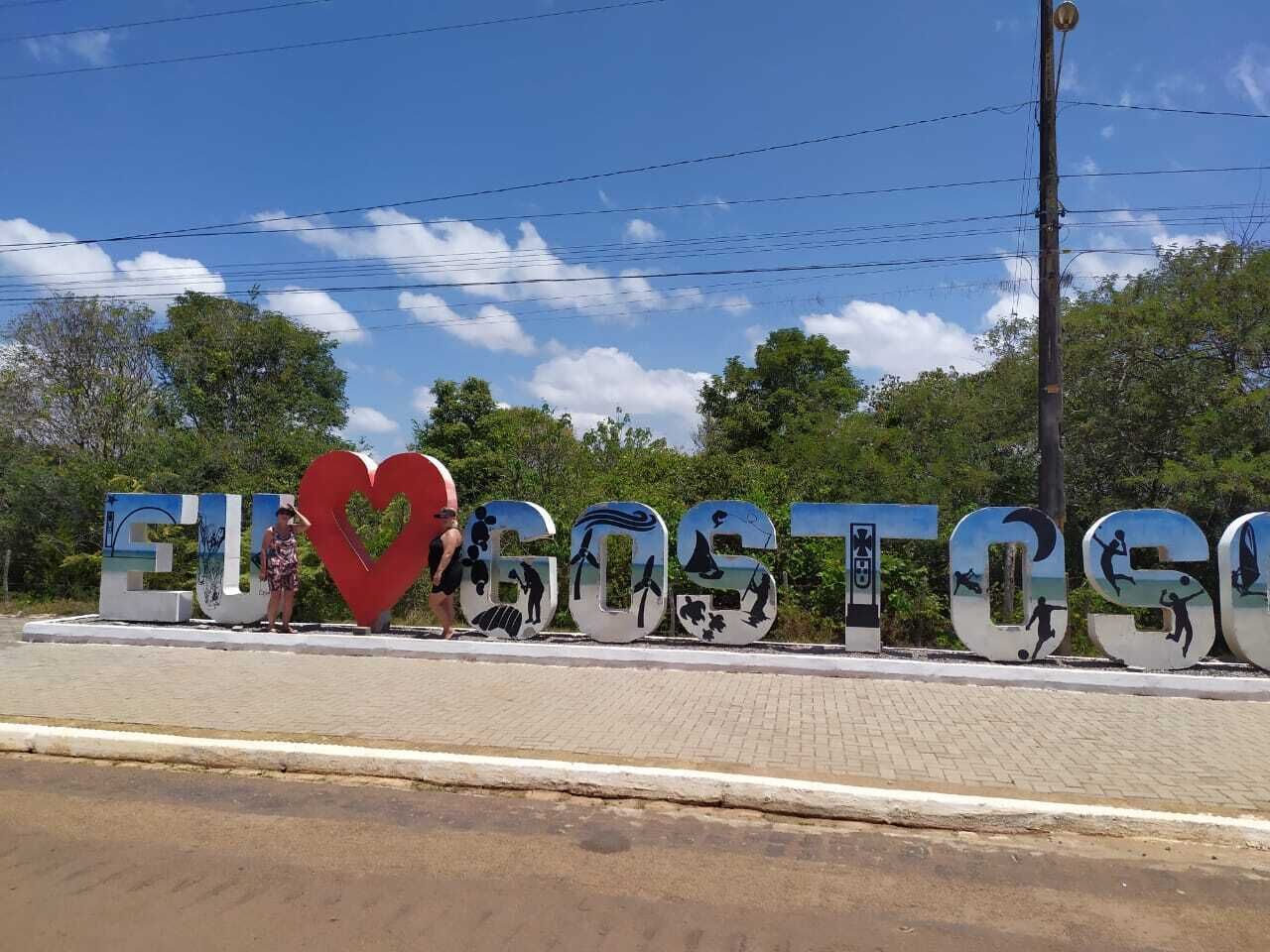 Um grande letreiro ao ar livre com as palavras EUROGOSTOS e um símbolo de coração, rodeado por vegetação e céu azul.