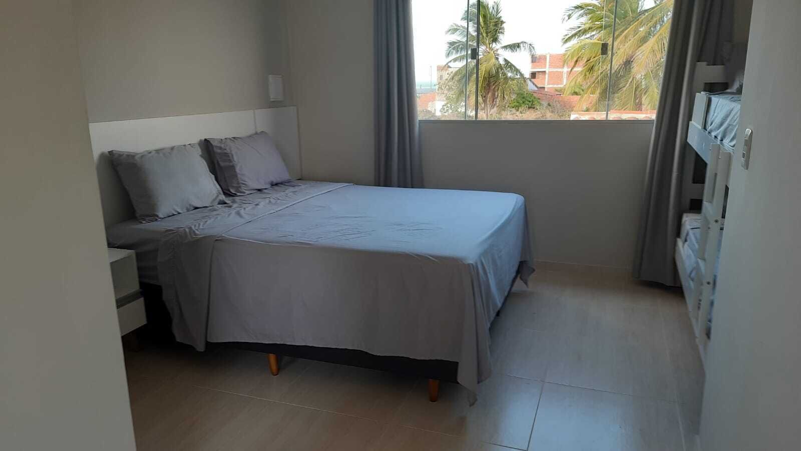 A small, neatly arranged bedroom with a bed, nightstand, and a window with a view of palm trees and buildings.
