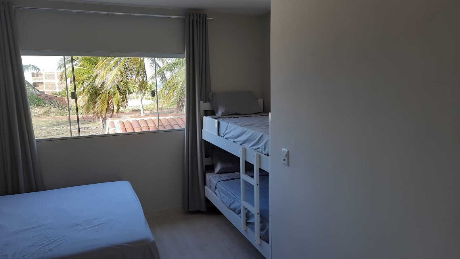 A small, single-room hotel room with a bed, a bunk bed, and a window with curtains.