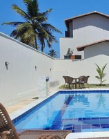 Una piscina con borde de azulejos, una pared blanca y un pequeño patio con dos sillas y una mesa.