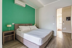 Un dormitorio con cama, mesita de noche, lámpara y pared verde.