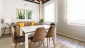 Een moderne woonkamer met een witte bank, bruine fauteuils, een witte tafel en twee schilderijen van cactussen aan de muur.
