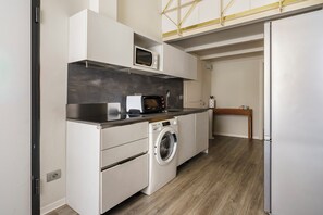 A compact kitchen with a washing machine, microwave, and a small table.