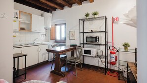 A compact kitchen with a dining table, chairs, a microwave, and a shelf with potted plants. - Chiasso degli Armati (Firenze)