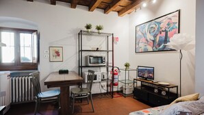 Habitación compacta con mesa de comedor, sillas, microondas, televisor pequeño y radiador.