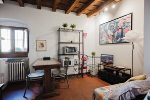 A compact room with a dining table, chairs, a microwave, a small TV, and a radiator. - Chiasso degli Armati (Firenze)